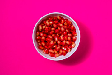 pomegranate seeds in a white bowl on a magenta background