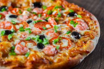 Pizza with Mozzarella cheese, olives, shrimps, tomato sauce, Spices and Fresh green onion. Italian pizza on wooden table background