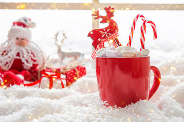 Obraz na płótnie Canvas Red cup with hot chocolate marshmallows on white window blanket, christmas composition