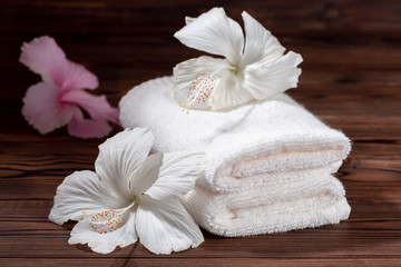 Fototapeta na wymiar spa composition of white cotton towels folded and flowers of hibiscus on wooden table, close up