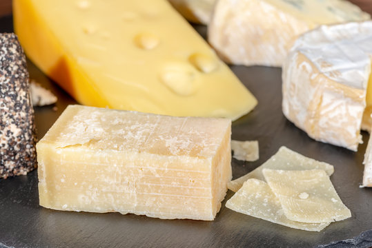 portion and slaced of fresh parmesan cheese and various types of cheese on black slate, close up