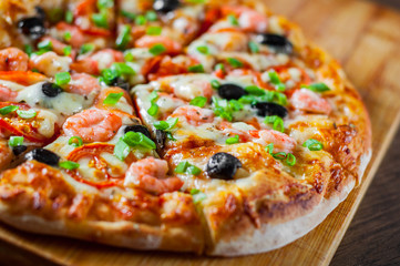 Pizza with Mozzarella cheese, olives, shrimps, tomato sauce, Spices and Fresh green onion. Italian pizza on wooden table background