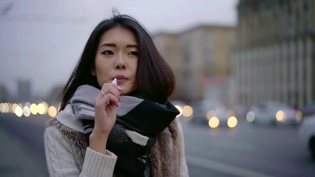 Portrait of a lovely urban brunette girl smoking iqos and drinking coffee from a cup outdoor.