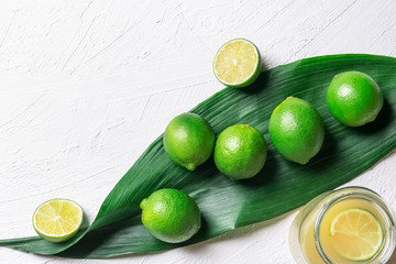 Limes on a big leaf and jar with juice. Fresh green citrus fruits. Healthy food.