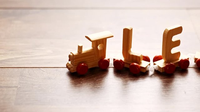Children vintage toy train going forward on wooden background. Kids railway made of wood letters running on the table. Hand moving toy train, child boy playing with toy rail road at home.