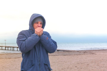 Man in a jacket by the sea warms frozen hands and waiting for someone.
