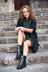 Young woman tourist in dress sitting at stone stair and playfully posing