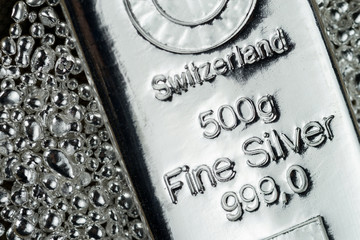 A cast silver bar weighing 500 grams and silver granules are isolated on a white background....