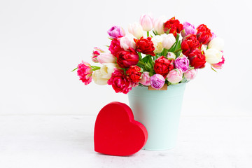 Fresh tulips flowers in pot with heart gift box over white table