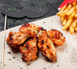 Fried chicken wings with baked potatoes and bbq sauce on craft paper on black background. Hot Meat Dishes. Top view
