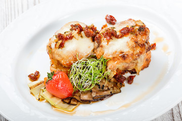 Meat steak wrapped in prosciutto with cheese, eggplant, dried tomatoes on plate on wooden background close up.  Hot Meat Dishes. Top view