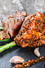 Grilled pork steaks with herbs, asparagus, garlic, mushrooms and potato fry on stone slate background on wooden background close up. Hot Meat Dishes. Top view, flat lay