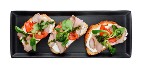 Breakfast sandwich with ham, tomatoes, cream cheese and spinach sauce on black plate isolated on white. Bruschettas on kitchen table. Healthy snack and appetizer top view, flat lay