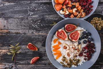 Rice coconut porridge with figs, berries, nuts, dried apricots and coconut milk in plate on rustic wooden background. Healthy breakfast ingredients. Clean eating, vegan food concept. Top view