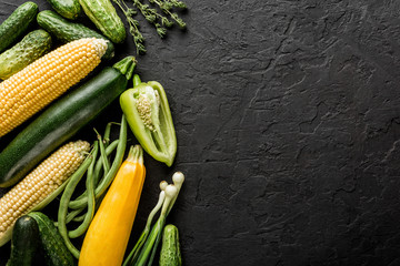 Healthy raw summer vegan vegetables and herbs, cucumbers, corn, pepper, zucchini, green beans on black stone background. Healthy food, clean eating, top view, flat lay