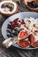 Rice coconut porridge with figs, berries, nuts, dried apricots and coconut milk in plate on rustic wooden background. Healthy breakfast ingredients. Clean eating, vegan food concept, close up