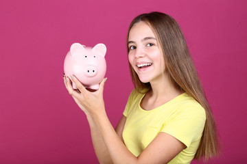 Young girl holding pink piggybank on pink background