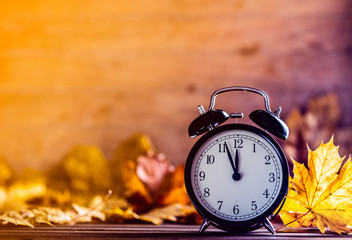 Vintage alarm clock and maple tree leaves on yellow wooden background with bokeh. Autumn season image style