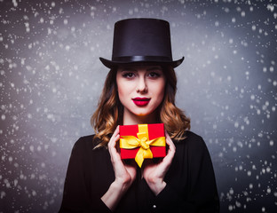 Style and mystique redhead girl in top hat with gift box on grey background