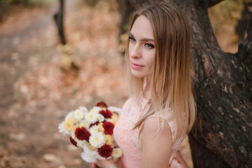Beautiful girl in pink dress with flowers in autumn forest.