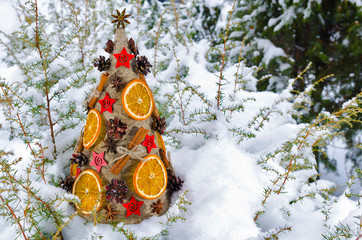 Необычная новогодняя ель, выполненная в стиле &laquo;арт-деко&raquo; украшенная сушеными апельсинами, сосновыми шишками и корицей на фоне заснеженной хвои.
