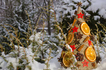 Необычная новогодняя ель, выполненная в стиле «арт-деко» украшенная сушеными апельсинами, сосновыми шишками и корицей на фоне заснеженной хвои. - obrazy, fototapety, plakaty