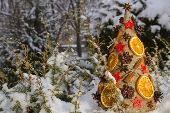 Необычная новогодняя ель, выполненная в стиле «арт-деко» украшенная сушеными апельсинами, сосновыми шишками и корицей на фоне заснеженной хвои.