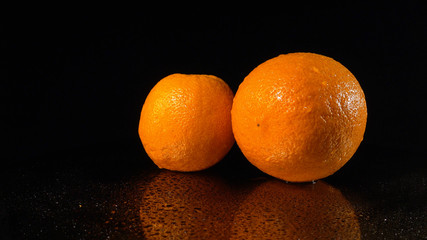 Ripe oranges on a mirror background. A fresh orange rotates on a wet mirror.