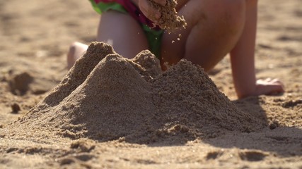 A girl of 4-5 years is building a sand castle. A child plays on the beach.