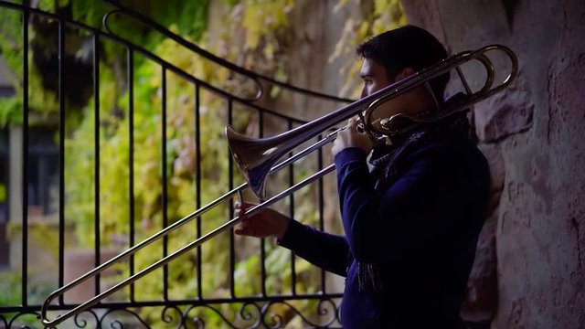 Side view shot of a brunet jazz player playing a song on trombone outdoor in a park.
