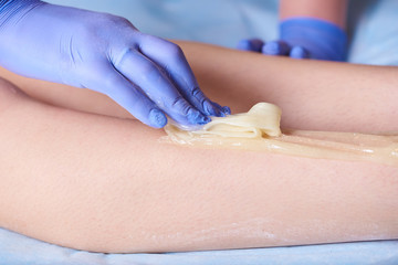 Naklejka premium Cosmetologist's hand with sugar wax doing depilation on legs