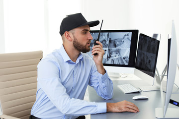 Male security guard with portable transmitter monitoring home cameras indoors