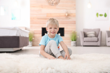 Fototapeta premium Cute little boy sitting on fur rug at home