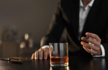 Man with glass of whiskey and cigar sitting at table, closeup. Space for text