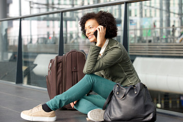  african american woman sitting on floor at station with luggage and talking on cellphone