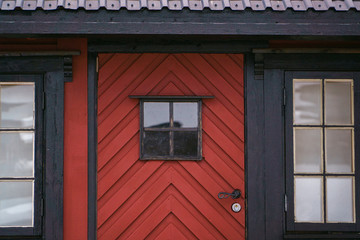 An old vintage wooden front door with window on a red country house. Facade exterior, closeup view. Retro countryside concept.
