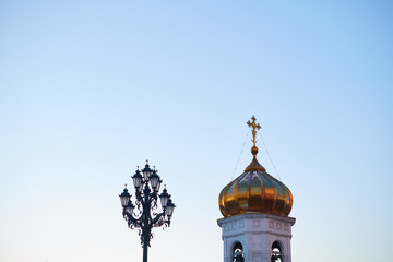 A golden dome and a cross of a chirch with a street lamp with blue sky on the background