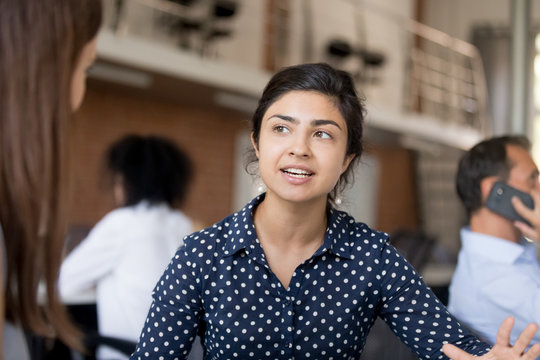 Attractive female Indian employee talking, discussing business strategy, project with colleague at workplace, mentor explaining task to trainee, businesswoman having conversation with intern close up