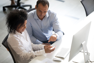 Diversity colleagues using smartphone together at workplace, checking social network, African...