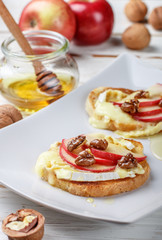 Bruschetta sandwiches with brie or Camembert cheese, apples, walnuts  and honey. Delicious healthy Breakfast in a white plate. Selective focus