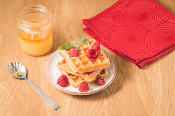 Waffles With raspberry in plate on a red napkin/waffles with raspberry in plate on a red napkin, and jar of honey on a wooden background, selective focus