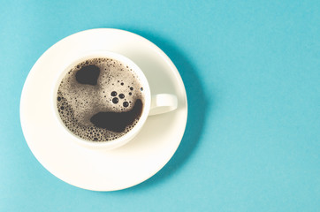 white cup of espresso with a skin on a blue background/white cup with a saucer full of black coffee with a skin on a blue background. Top view