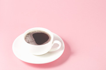 white cup with a saucer on a pink background/white cup of espresso with a foam on a pink background, selective focus and copy space