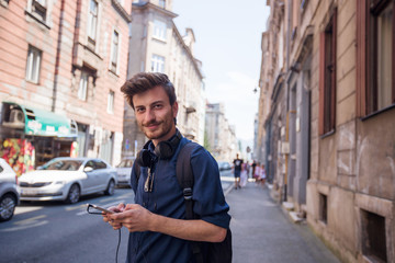 Portrait of cheerful young tourist using phone on the street