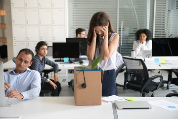 Fototapeta premium Desperate dismissed woman holding head in hands at workplace, upset female employee pack belongings in cardboard box, feeling stressed about job loss, unexpected undeserved dismissal, discrimination