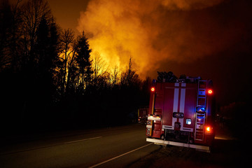 Forest fire with smoke and a road with fire engine at night, view from the distance