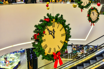 The New Year's clock is decorated with green branches and hangs on a rope in a store in a shopping center and foreshadow the coming of the new year.
