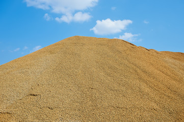 A view to the top of a mountain of sand with blue sky on the background on a sand career