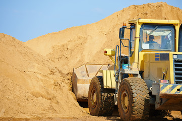 Excavator or digger working in a career with a mountain of sand on the background
