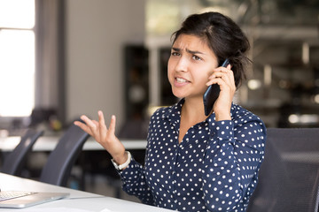 Outraged attractive Indian female employee talking by phone, arguing with client or customer,...
